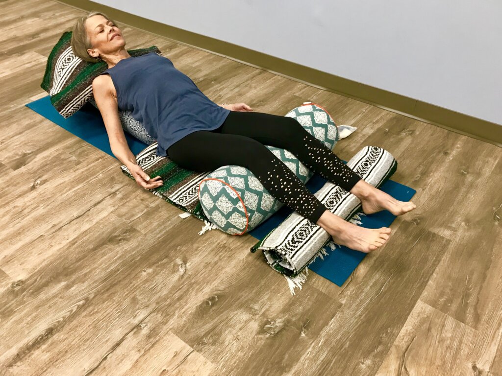 Moya McGinn Mathews demonstrates in a restorative yoga heart opener reclined on a bolster with knees supported on another bolster.