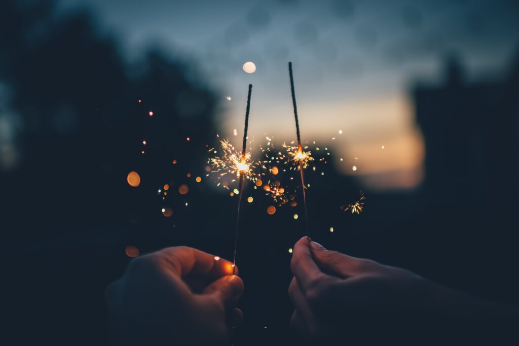 Two hands hold burning sparklers in the dark on New Year's Eve.