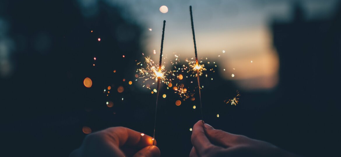 Two hands hold burning sparklers in the dark on New Year's Eve.