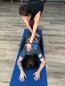 Holly Schramm provides gentle hands-on assist with one hand on shoulder and the other on a hip in child's pose.